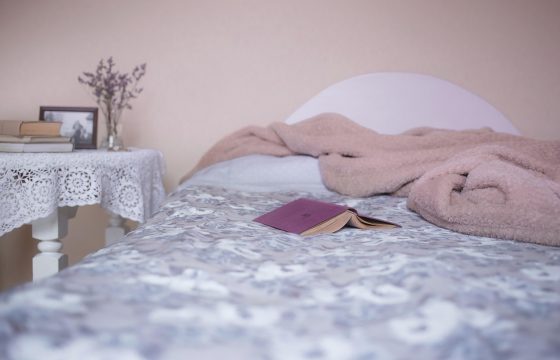 夜晚卧室床头灯下，读者靠在枕头上用手机阅读文字版，屏幕光映在脸上